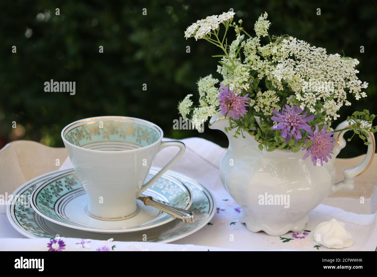 Bouquet von Wiesenblumen in Milchkanne und Jahrgangskaffee tasse als Sommerdeko Stockfoto