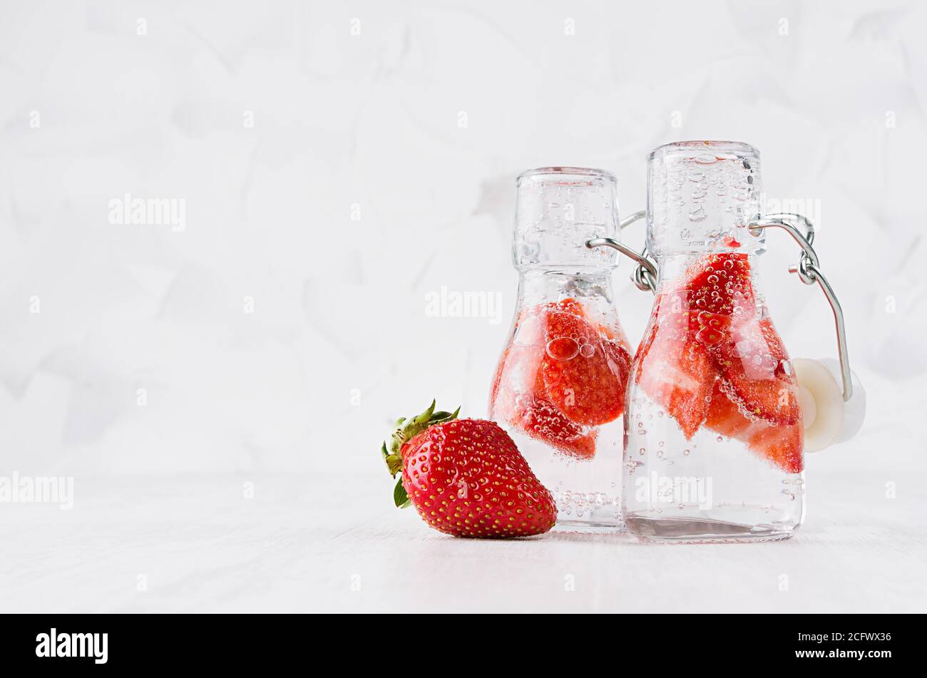 Natürliche Bio-Cocktails mit Erdbeere, kohlensäurehaltiges Wasser in zwei Yoke-Flaschen auf hellweißem Holzbrett und Wand, Kopierraum. Stockfoto