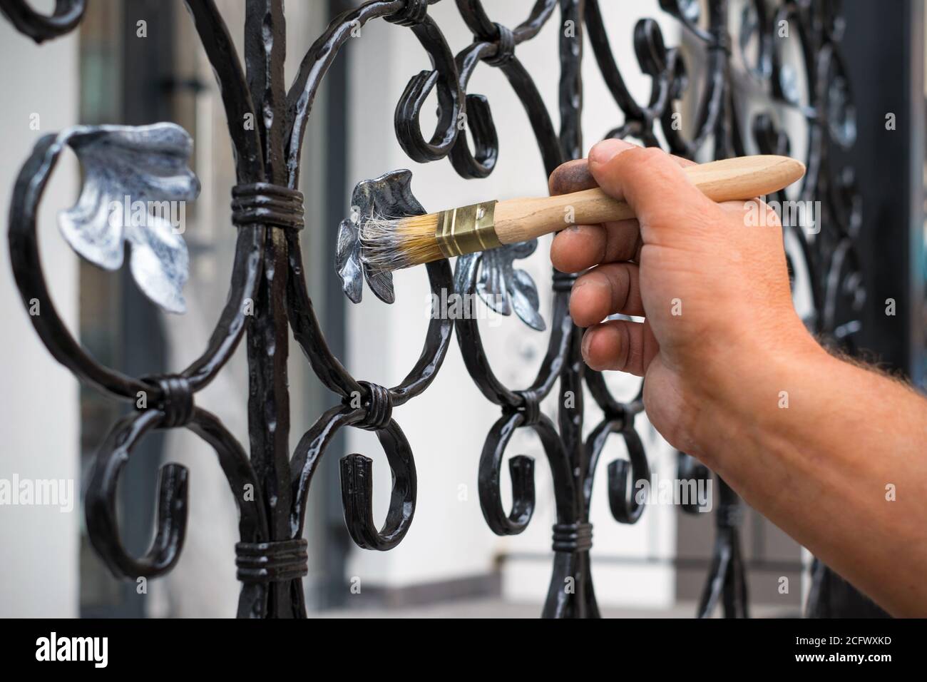 Hand des Auftragnehmers mit Pinsel, die Metallzaun malen. Stockfoto