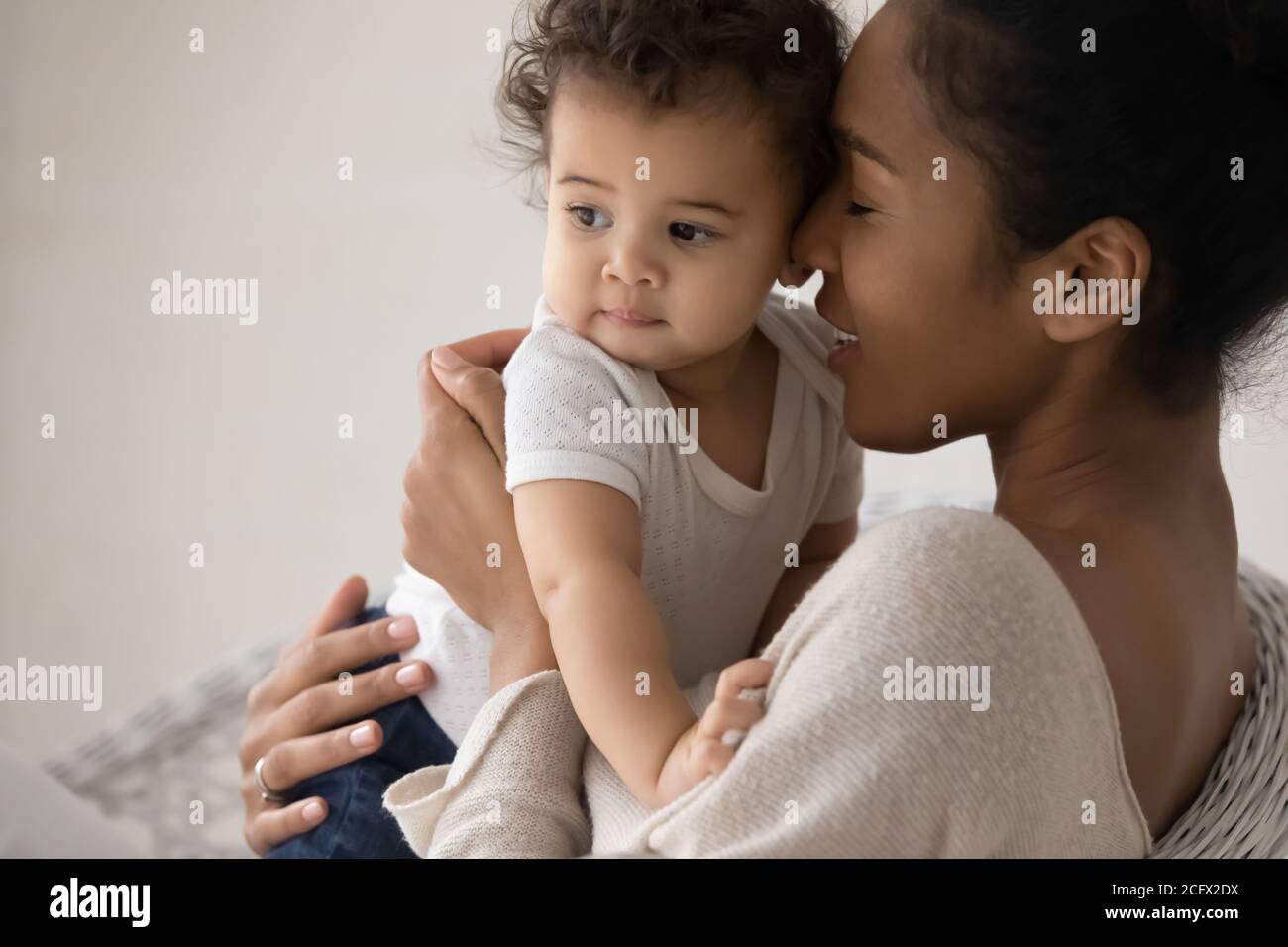 Fürsorgliche junge Mischlingsmutter kuscheln wenig biracial Baby. Stockfoto
