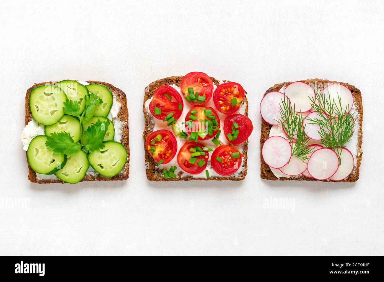 Verschiedene Sandwiches zum Frühstück mit Scheibe Vollkornbrot, Frischkäse, Gurken, Radieschen, Kirschtomaten, garniert mit Dill Stockfoto