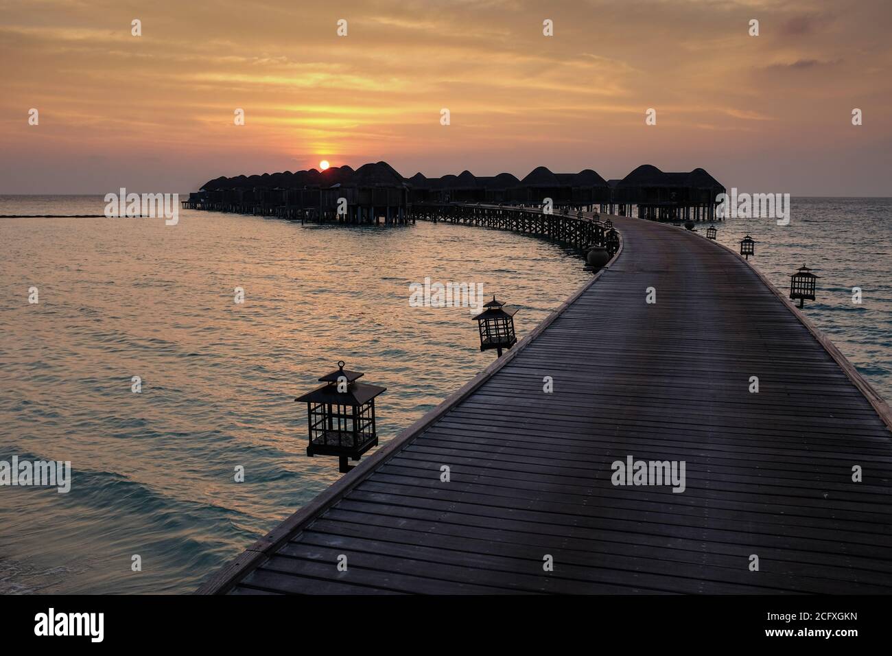 Ein gebogener Steg führt zum Meer, um eine Gruppe von Gästezimmern oder Überwasser-Villen in einem Luxus-Hotelresort auf den Malediven zu erreichen. Stockfoto