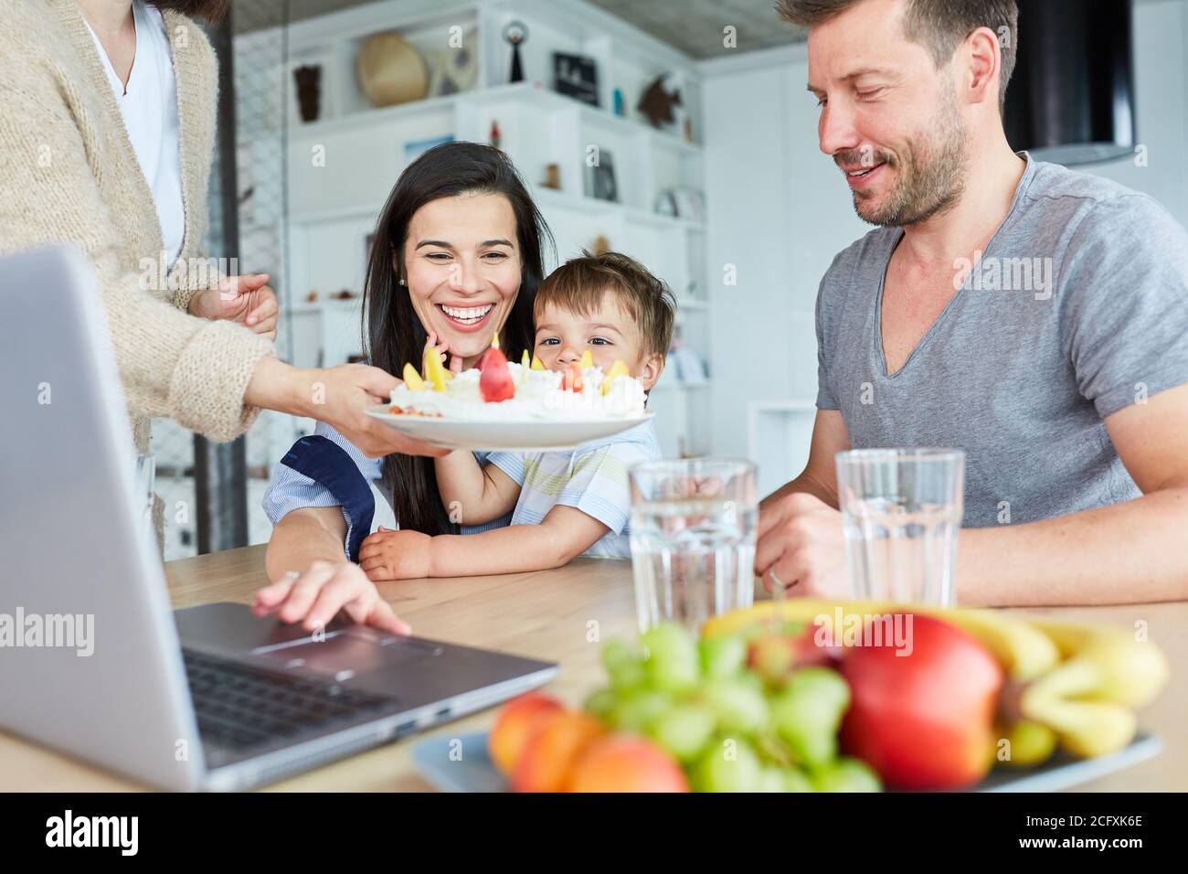 Familie mit Kind feiert Geburtstag mit einem hausgemachten Kuchen in Video-Chat Stockfoto