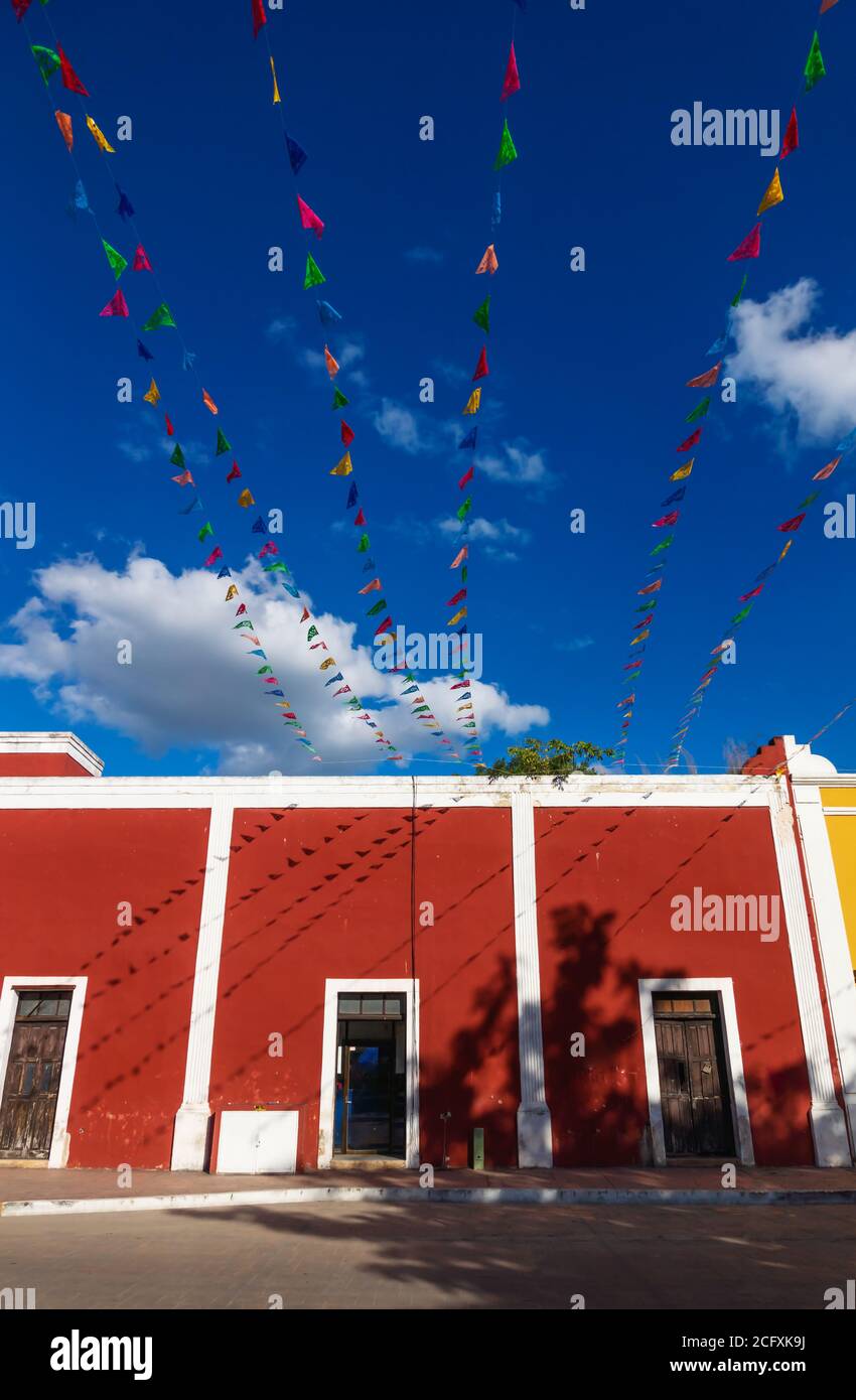 Lebhafte Fahnenketten über hellblauem Himmel mit weißen Wolken entlang rotem Kolonialgebäude, Valladolid, Yucatan, Mexiko Stockfoto
