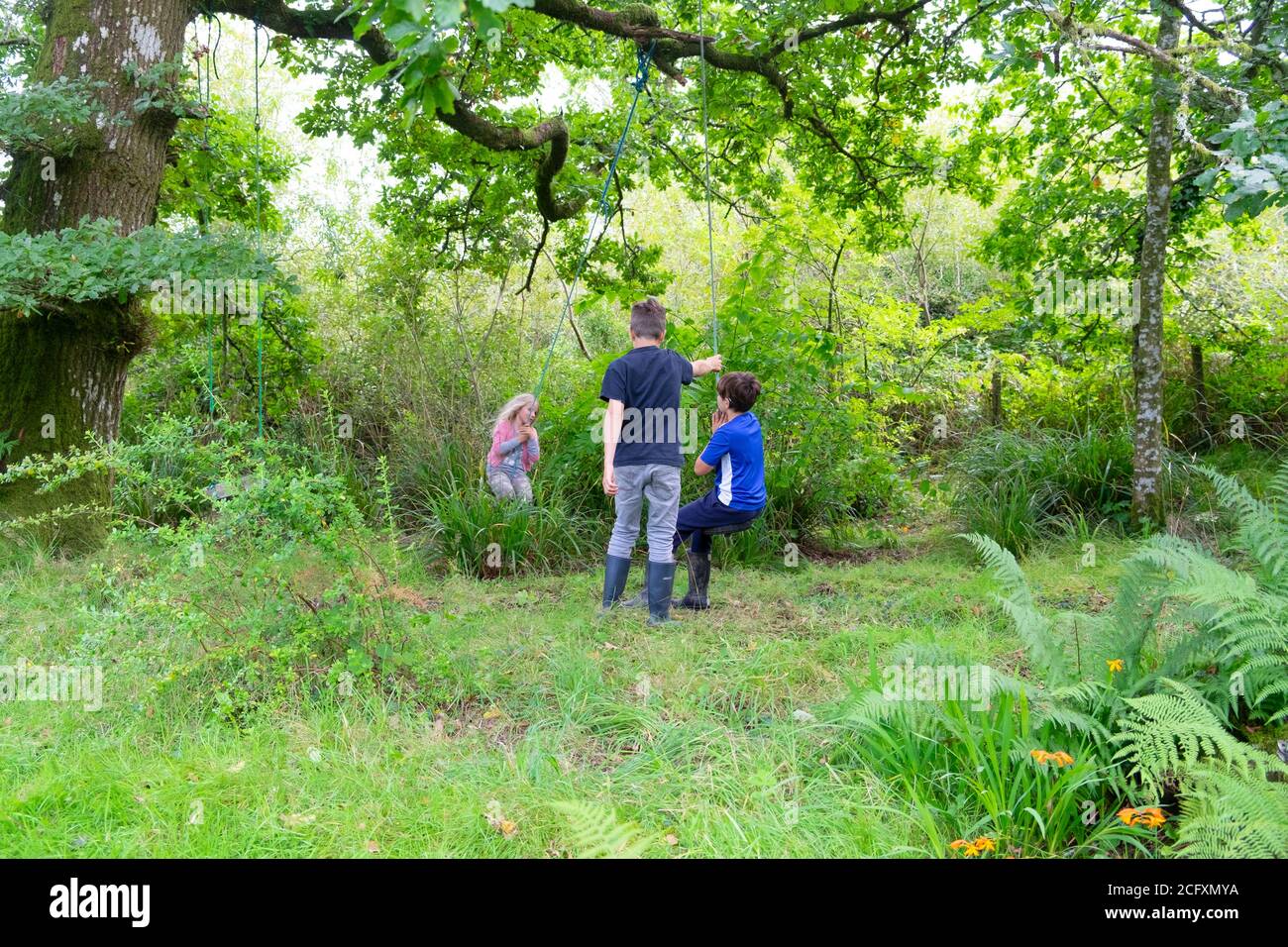 Kinder Kinder spielen draußen auf dem Land auf Gartenschaukel im Sommerurlaub 2020. August in Carmarthenshire Wales UK KATHY DEWITT Stockfoto