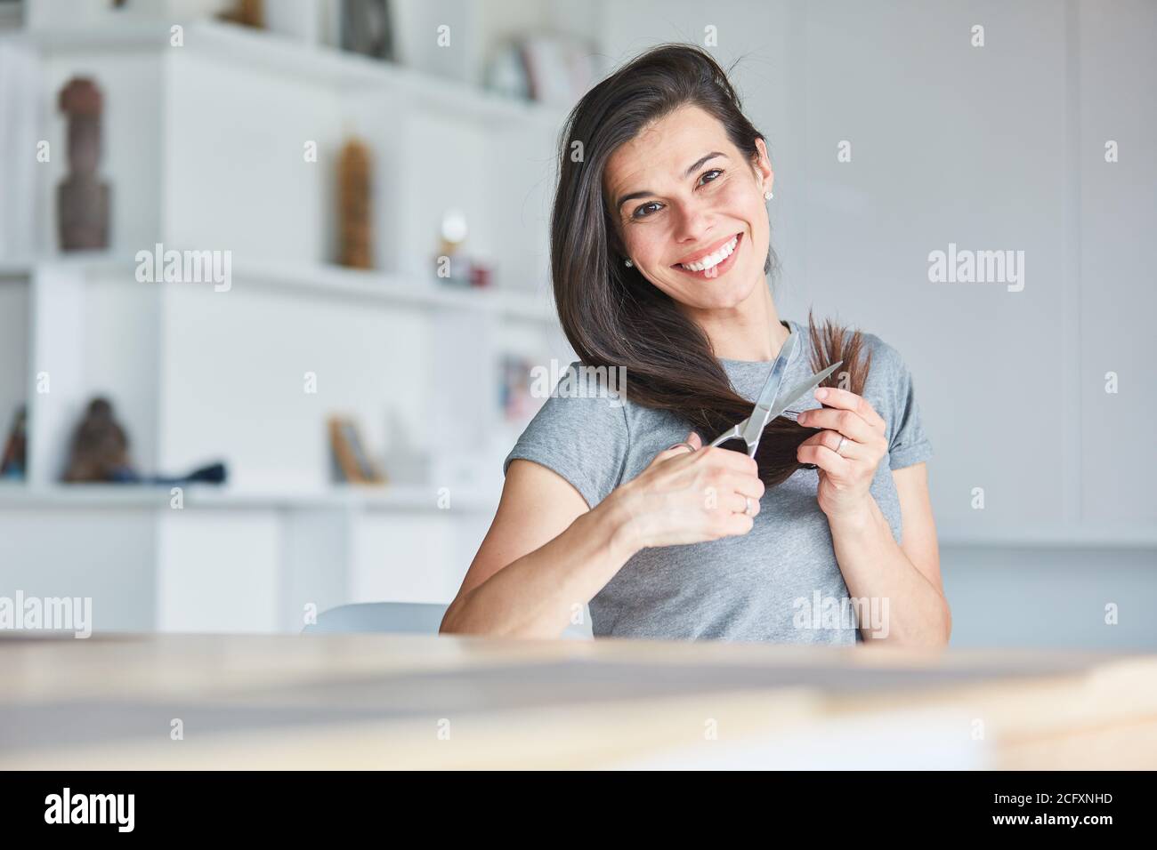 Glückliche junge Frau mit Schere zu Hause beim Schneiden sie Langes Haar für sich Stockfoto
