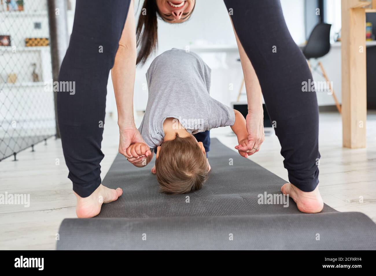 Mutter hilft dem Kind, in einem Fitnessstudio zu Hause Saltos zu machen Mat Stockfoto