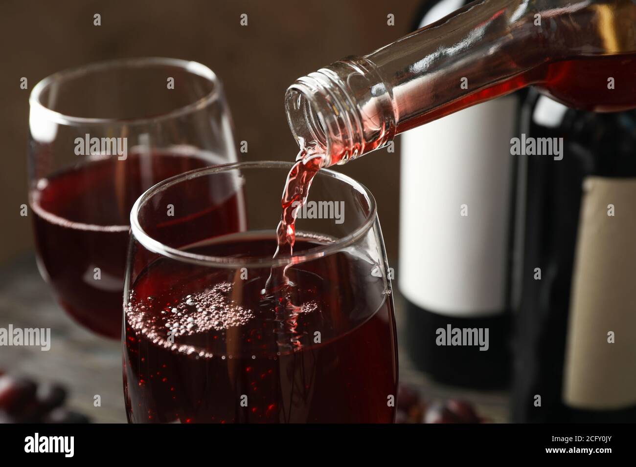 Wein wird aus einer Flasche in Glas auf Holztisch gegossen, close up Stockfoto