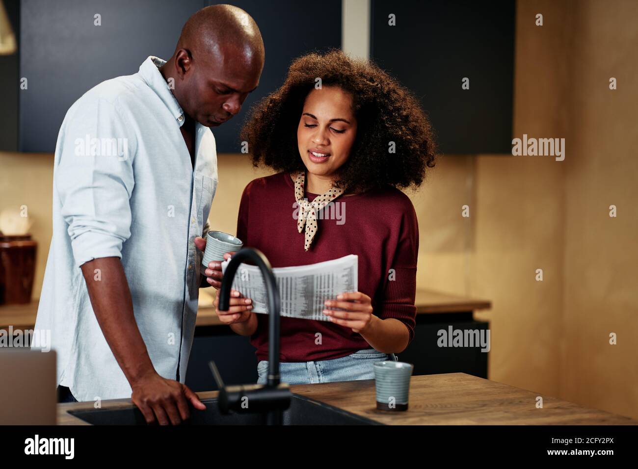 Junges afroamerikanisches Paar, das zusammen in ihrer Küche steht und liest Die Finanzseiten einer Zeitung Stockfoto