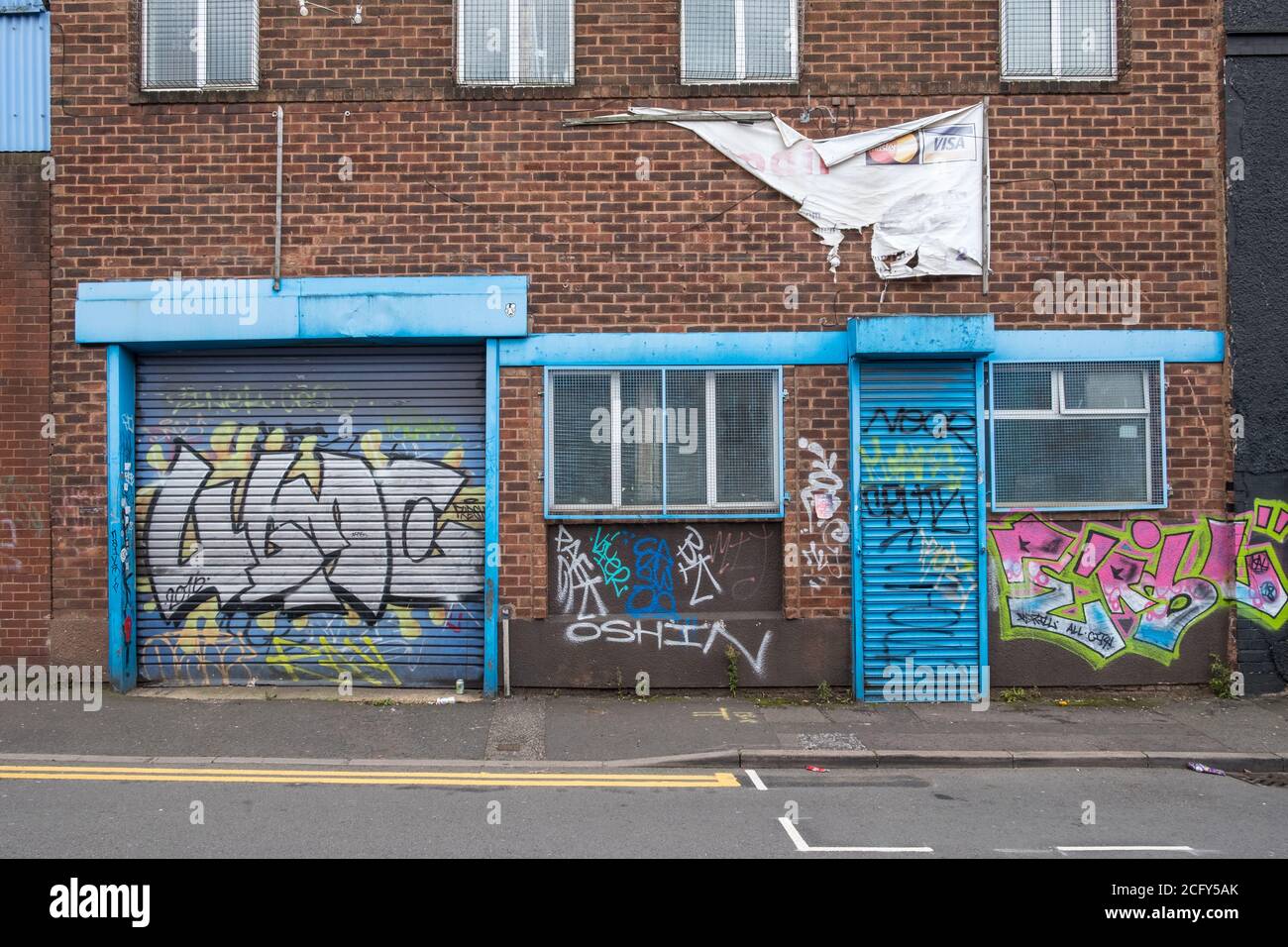 Kleine Werkstatt oder Fabrikanlage in Digbeth, Birmingham mit blauen Rollläden, die mit Street Art Graffiti bedeckt sind Stockfoto