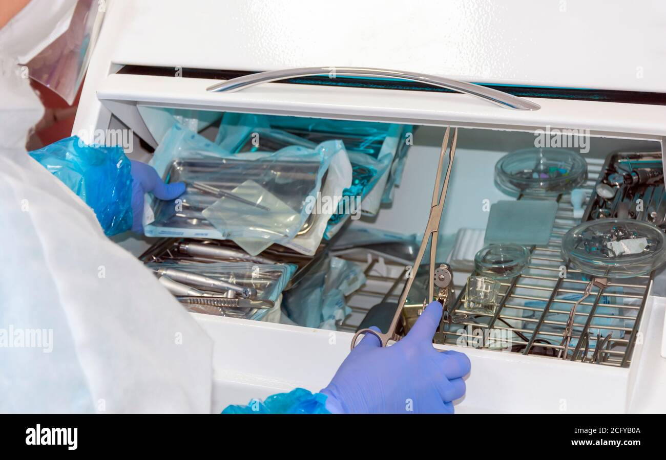 Die Krankenschwester entfernt medizinische Instrumente aus dem ultravioletten Schrank für Desinfektion in der Zahnarztpraxis unter Quarantänebedingungen Stockfoto