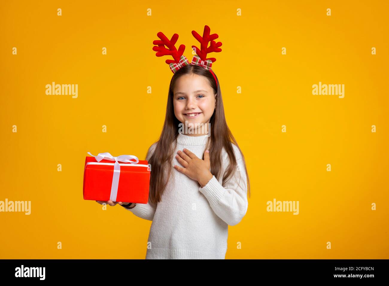 Frohe Feiertage. Lächelndes Mädchen mit Hörnern in Pullover hält Geschenk in der Hand Stockfoto