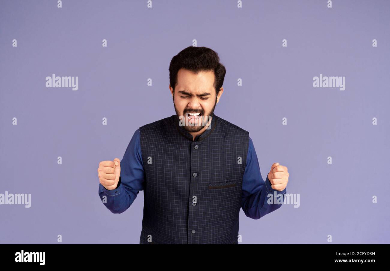 Wütender indischer Mann, der sich vor Wut die Fäuste zusammenhält und anschreit Lila Hintergrund Stockfoto