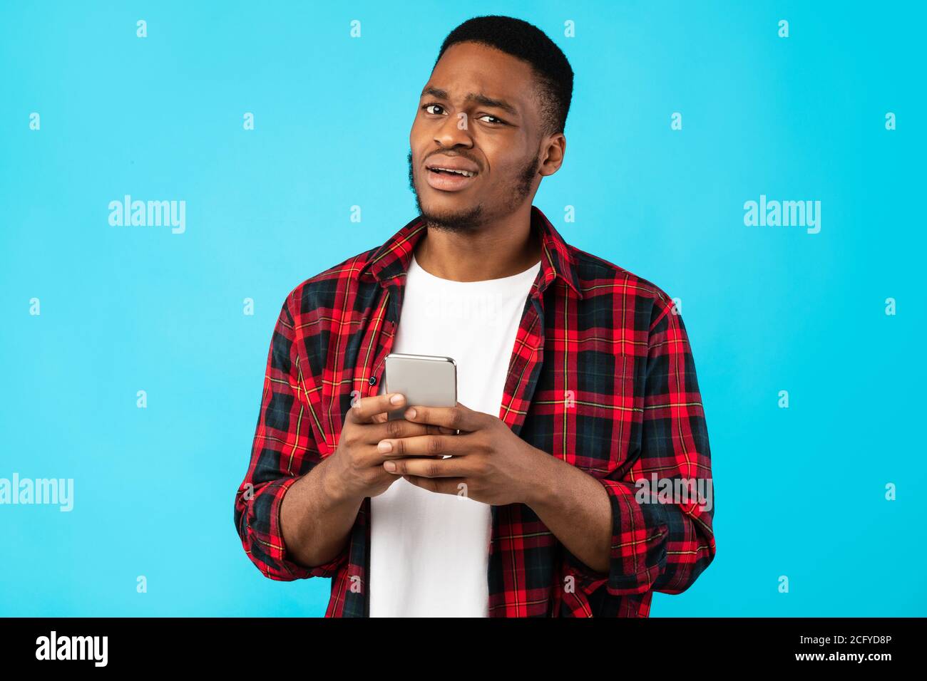 Unsicher Black Man Holding Handy Posiert Über Blauen Hintergrund Stockfoto