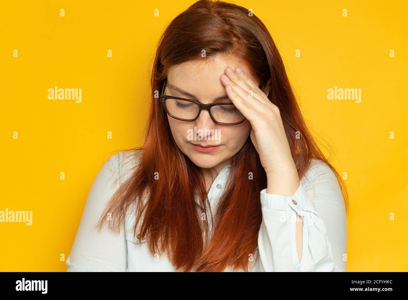 Unglückliche junge Frau mit roten langen Haaren und Brille leidet  Kopfschmerzen, Migräne auf einem gelben Wandhintergrund. Stress, Müdigkeit  Menschen Konzept. Hände auf dem Kopf Stockfotografie - Alamy