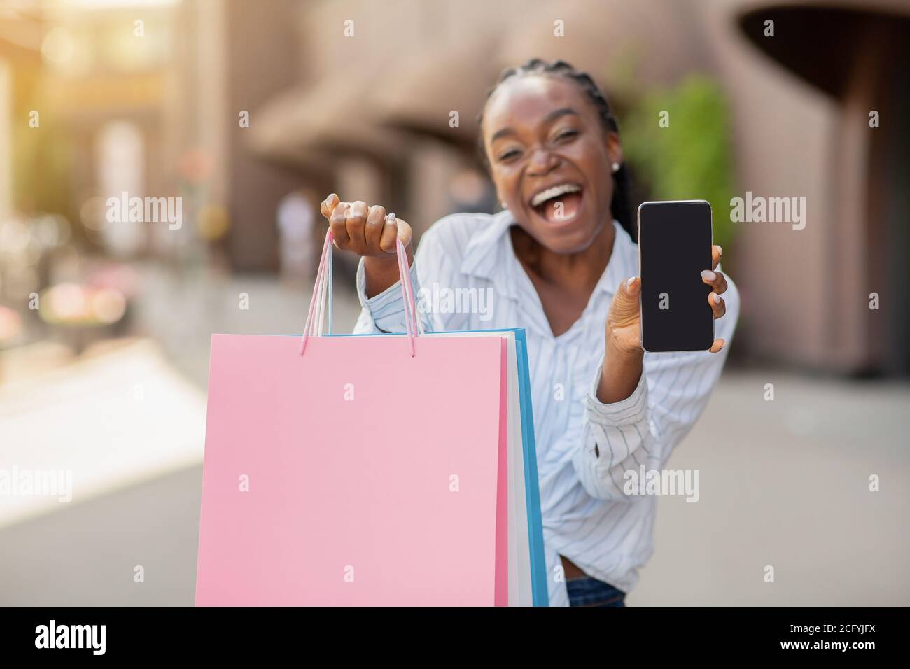 Geschenk und Bonus für mobile Benutzer. Shopper hält Einkaufstaschen, zeigt Kamera Smartphone Stockfoto