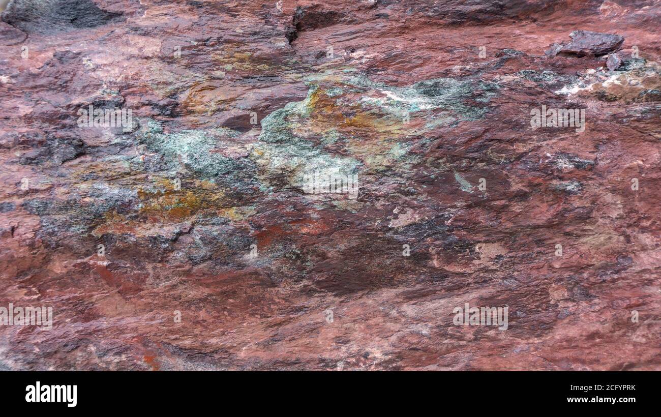 Hintergrund aus rotem Jaspis mit hellen Spritzern von lila, türkis und orange Mineral. Steintextur aus Gabbro-Diabase. Felsbrocken aus rotem Jaspis in Stockfoto