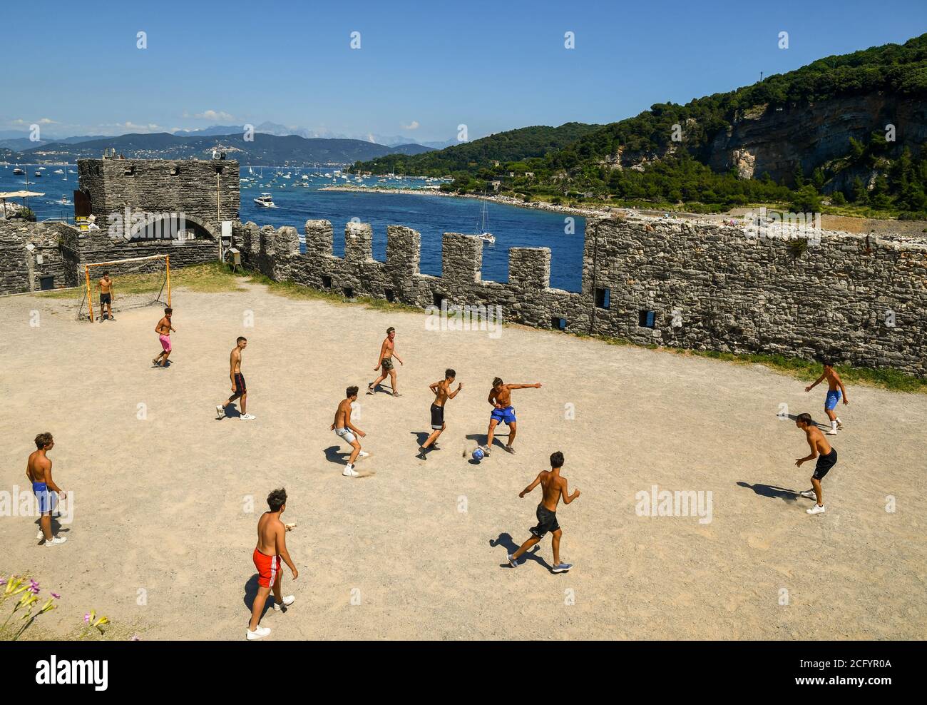 Eine Gruppe von Jugendlichen spielt Fußball im Park der Kirche St. Peter mit der Insel Palmaria im Hintergrund, Porto Venere, La Spezia, Italien Stockfoto