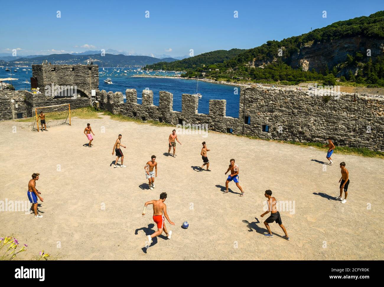 Eine Gruppe von Jugendlichen spielt Fußball im Park der Kirche St. Peter mit der Insel Palmaria im Hintergrund, Porto Venere, La Spezia, Italien Stockfoto