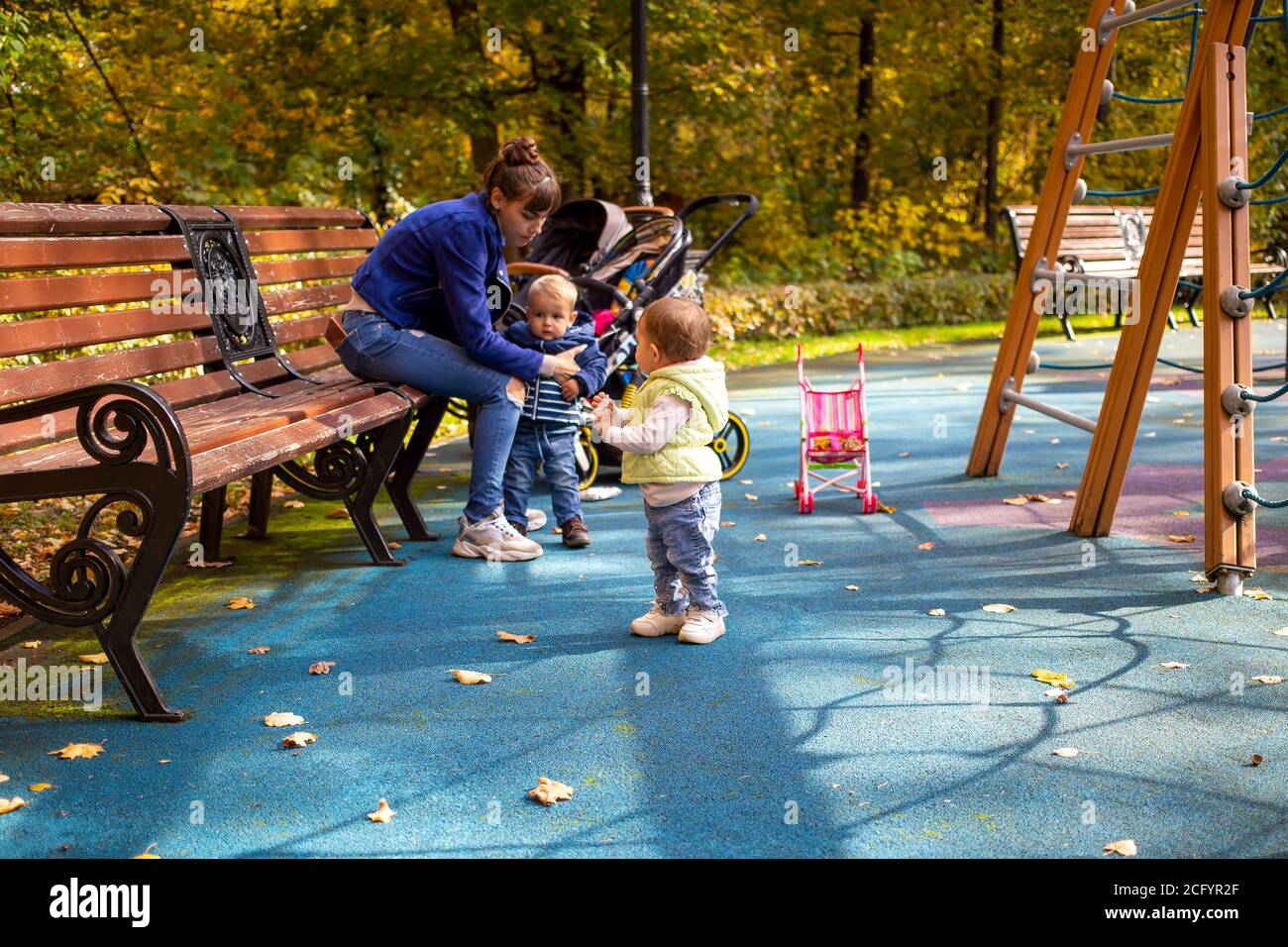 Mutter spielt mit Kindern Kleinkinder im Herbstpark in Der Spielplatz an einem sonnigen Tag Stockfoto
