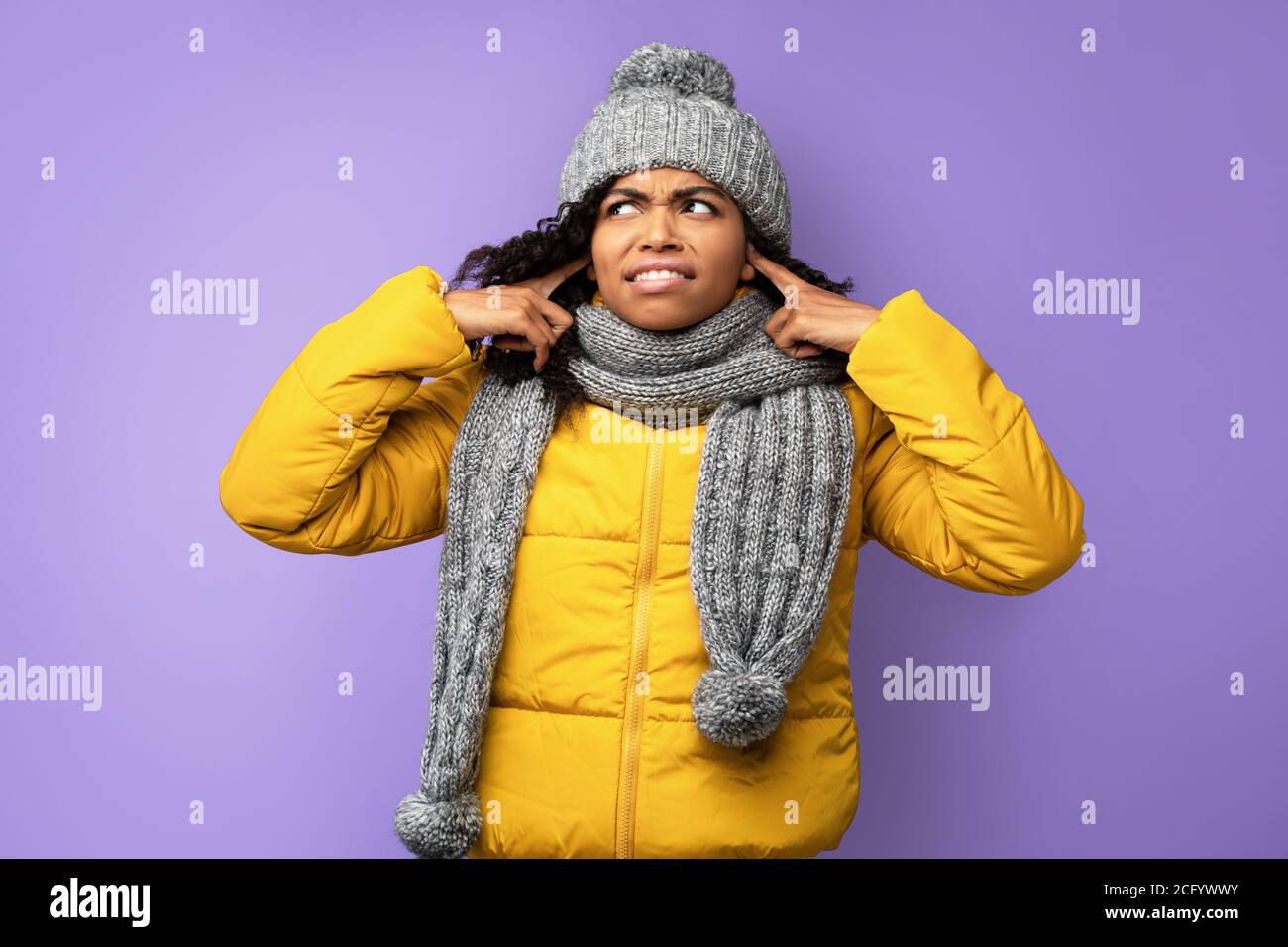 Unzufriedene Afrikanische Frau In Winterkleidung Verstopfte Ohren, Lila Hintergrund Stockfoto