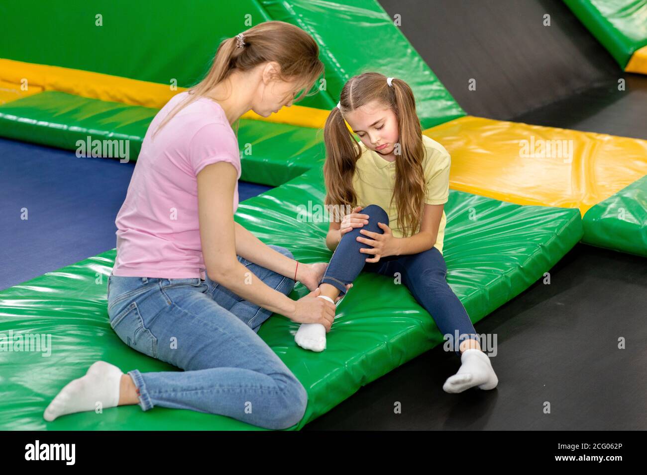 Trampolinspringen Unfall. Mutter und Kind mit Fußverletzung sitzen auf dem Trampolin auf dem Kinderspielplatz, innen Stockfoto