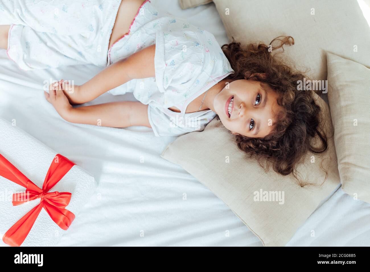 Schöne kleine lockige Mädchen im Schlafzimmer auf dem Bett schlafen Mit Geschenk Stockfoto