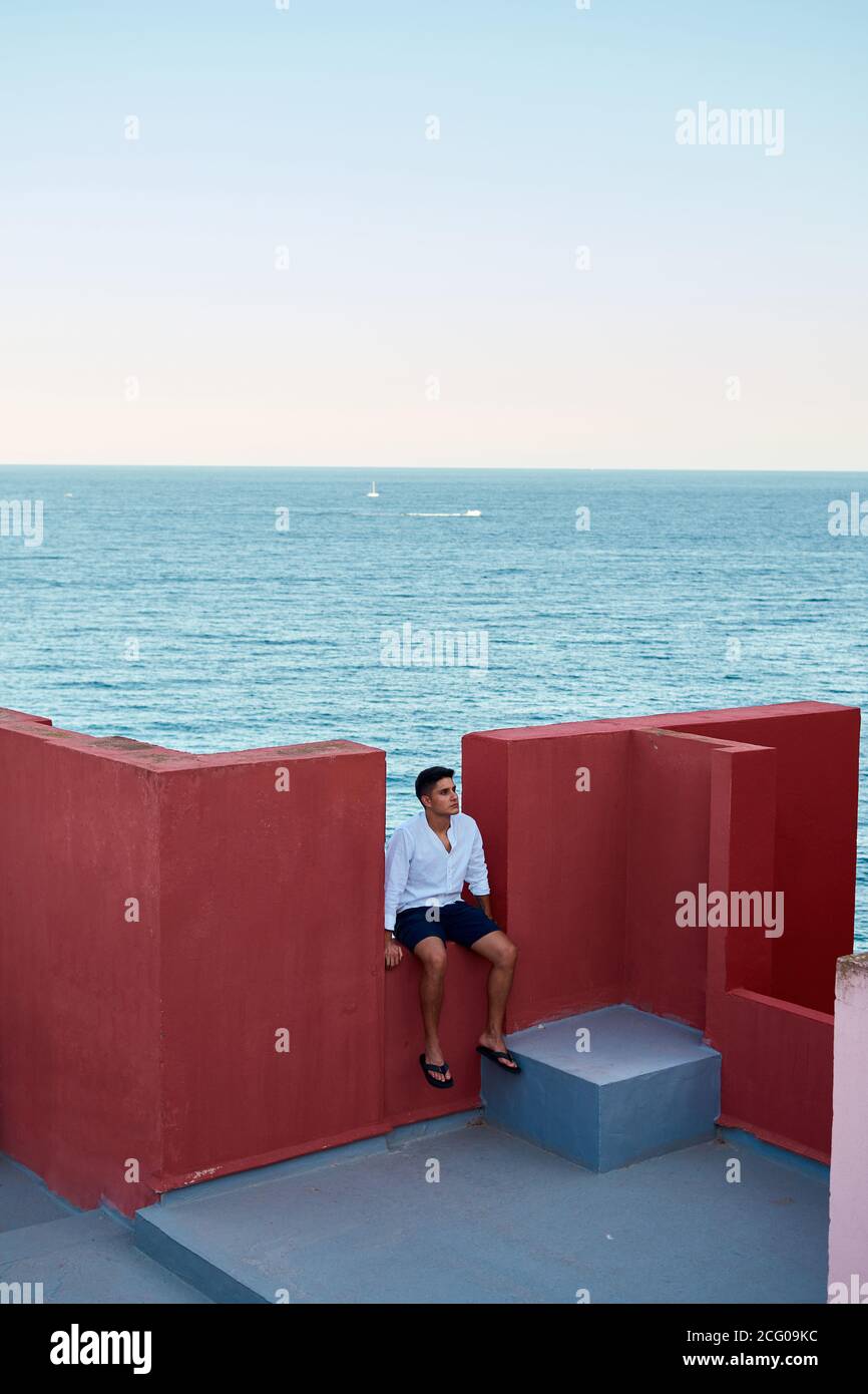 Junger lateinischer Mann meditativ in einem roten Gebäude, Meer im Hintergrund Stockfoto
