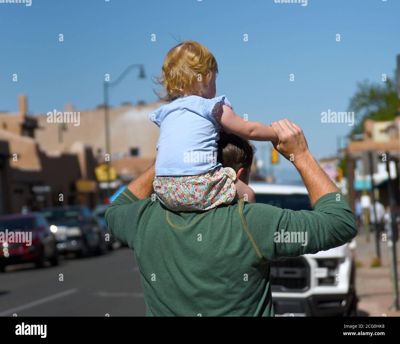 Ein Mann trägt seine junge Tochter auf seinen Schultern, während sie einen Bürgersteig in Santa Fe, New Mexico, hinuntergehen. Stockfoto