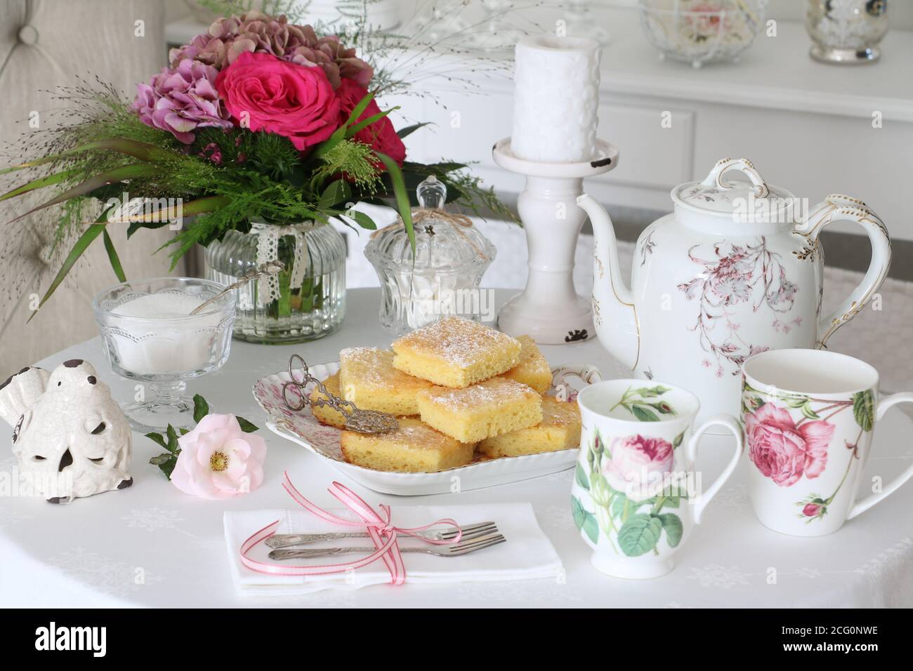 Tischdekoration mit Kuchen, Tassen mit Rosenverzierung und Blumenstrauß Stockfoto