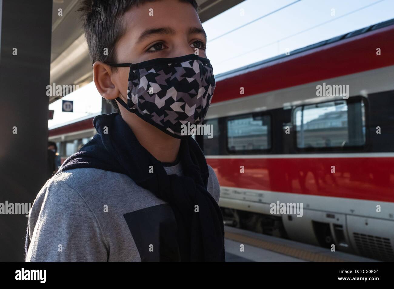 Nahaufnahme eines männlichen kaukasischen Kindes mit Gesichtsmaske als Schutz vor einer Coronavirus-Infektion. Er steht am Bahnhof. Stockfoto