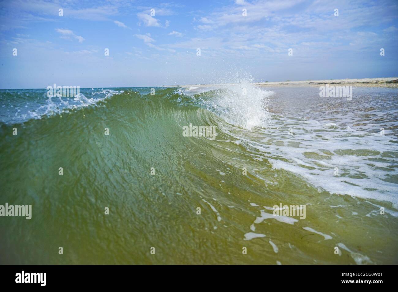 Eine azurblaue Meereswelle mit einem weißen Kamm läuft an Land. Stockfoto