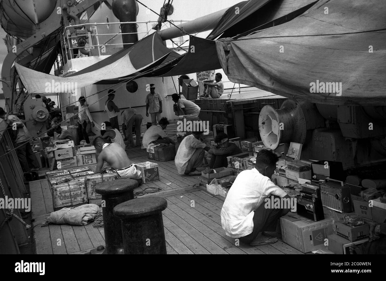 AJAXNETPHOTO. 1964. SINGAPUR, SINGAPUR. - ZOLLFREI - LOKALE HÄNDLER, DIE STEUERFREIE JAPANISCHE ELEKTRONIK- UND KAMERAWAREN VERKAUFEN, LEGEN IHRE WAREN AUF DEM HAUPTDECK EINES FRACHTSCHIFFES AB. FOTO: JONATHAN EASTLAND/AJAX REF: M120642 100 Stockfoto