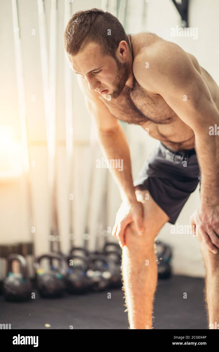 Aufnahme eines jungen Mannes in Sportkleidung, der sich mit den Händen auf den Knien im Fitnessstudio beugte. Fitness-Mann, der nach intensivem Cross-Fit-Training müde aussieht Stockfoto