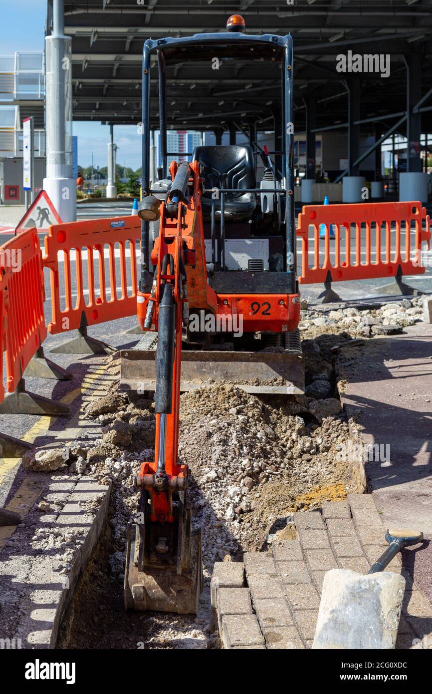 Ein kleiner Bagger gräbt den Bürgersteig während der Bodenarbeiten Stockfoto