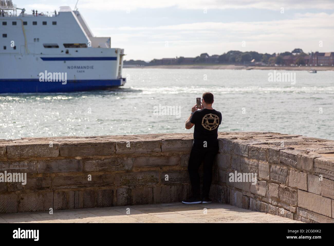 Ein Mann, der sein Mobiltelefon oder Handy benutzt Machen Sie ein Foto von einer vorbeifahrenden Fähre am Am Meer Stockfoto