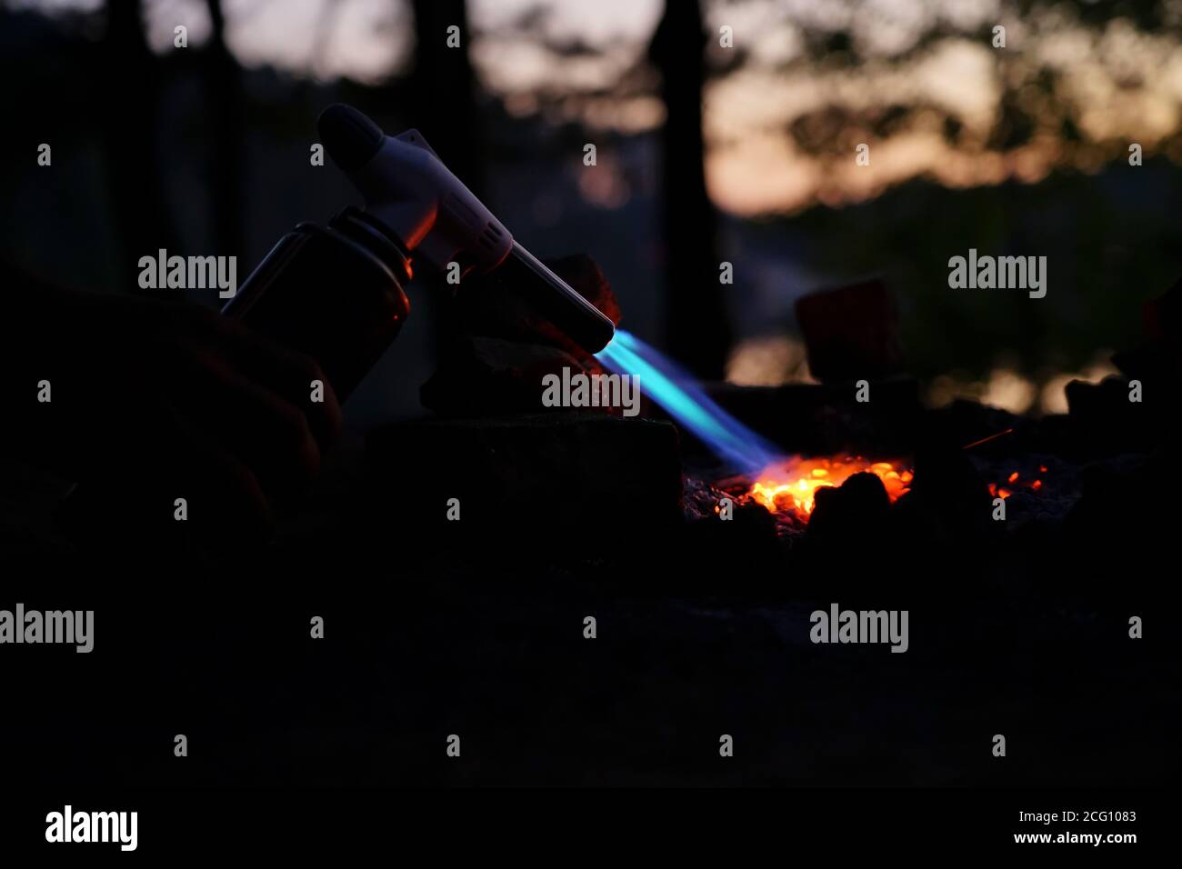 Hand hält Manul Gasbrenner in der Nähe von Brennholz in der Nacht Stockfoto