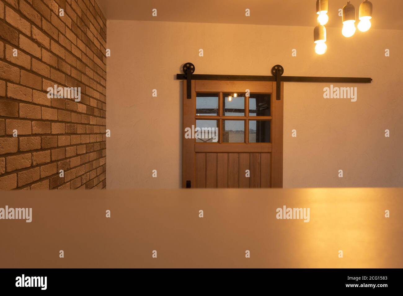 Holzschiebetür mit Vintage-Armaturen, ungewöhnlicher Betonbeleuchtung und Ziegelwand. Dachboden innen. Stockfoto