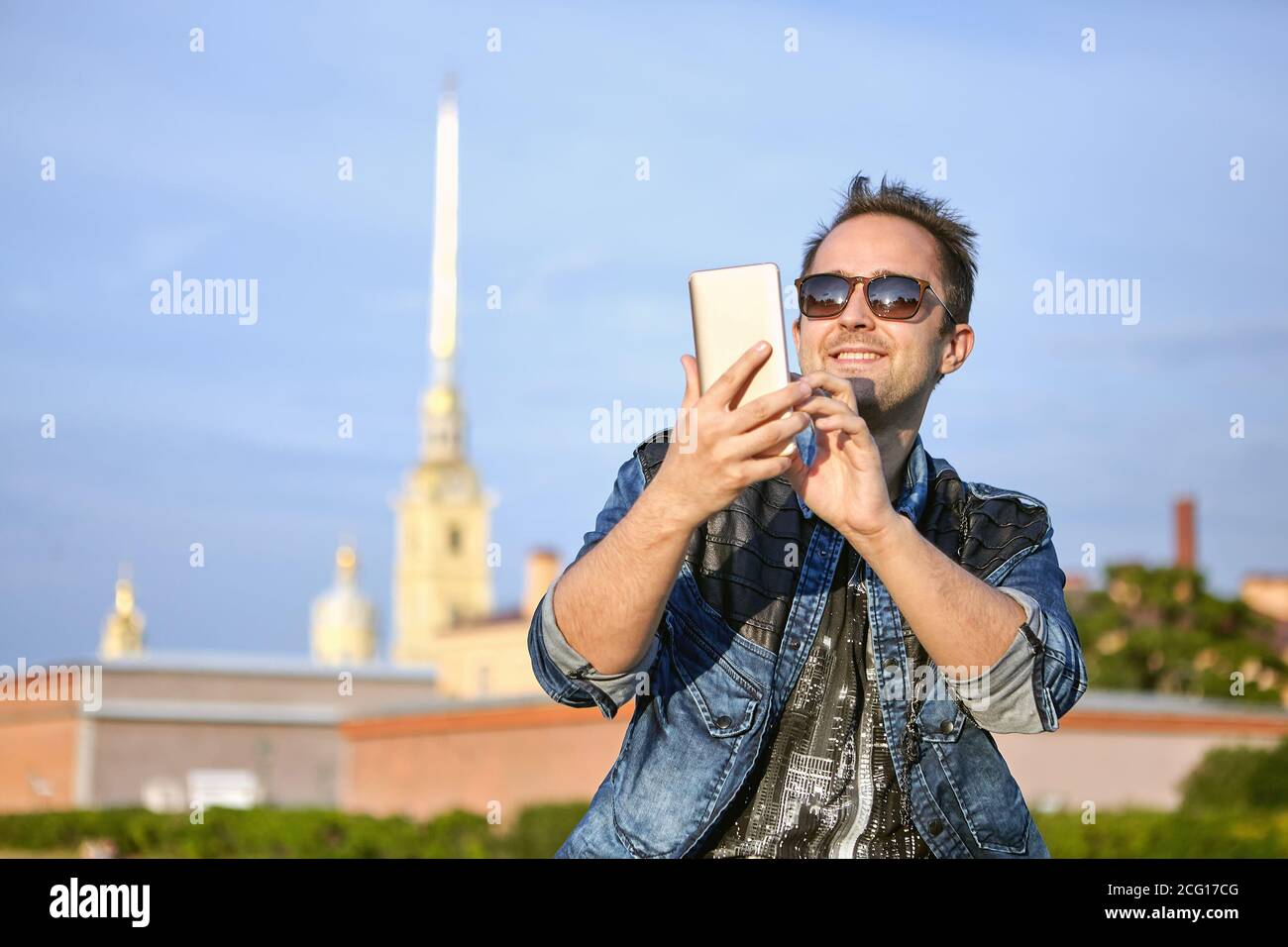 Junger lächelnder Mann schreibt eine Nachricht auf dem Bildschirm des Smartphones auf dem Hintergrund des historischen Zentrums von Sankt Petersburg, Russland. Stockfoto