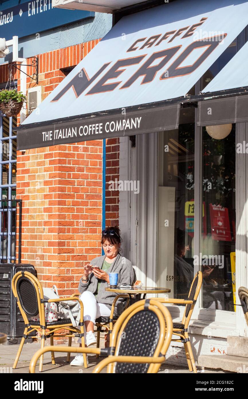 Frau, die draußen im Café Nero mit dem Handy sitzt Stockfoto