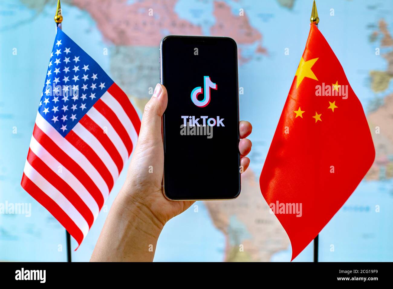 Calgary, Alberta, Kanada. September 2020. Eine Person, die ein iPhone mit dem TikTok App-Bildschirm neben einer USA- und China-Flagge auf einer Weltkarte hält. Stockfoto