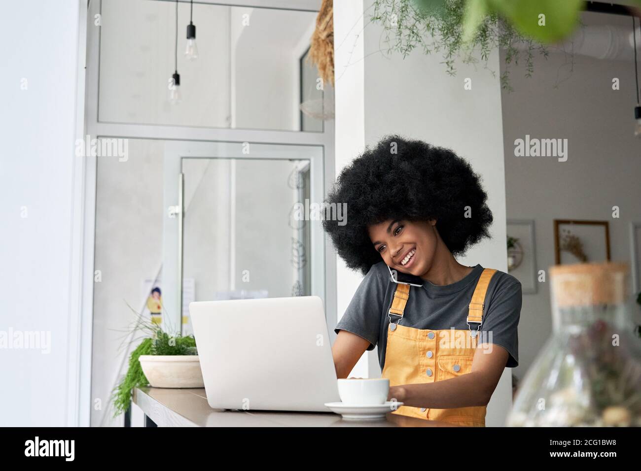 Glückliche junge afroamerikanische Frau, die im Café mit einem Laptop telefoniert. Stockfoto
