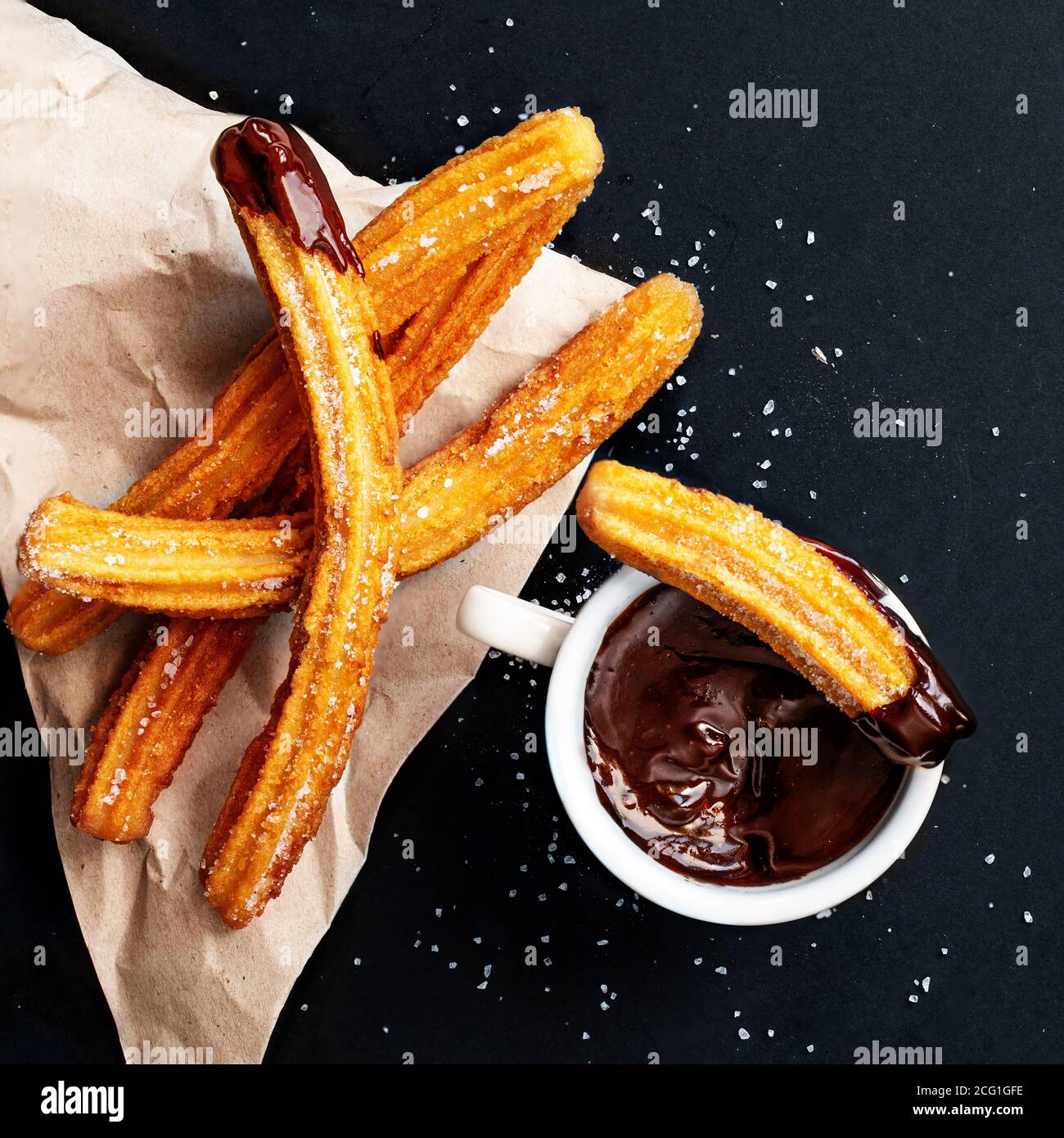 Churros mit Zucker in Schokoladensauce auf schwarzem Hintergrund getaucht. Churro-Sticks. Gebratenes Teiggebäck, Draufsicht Stockfoto