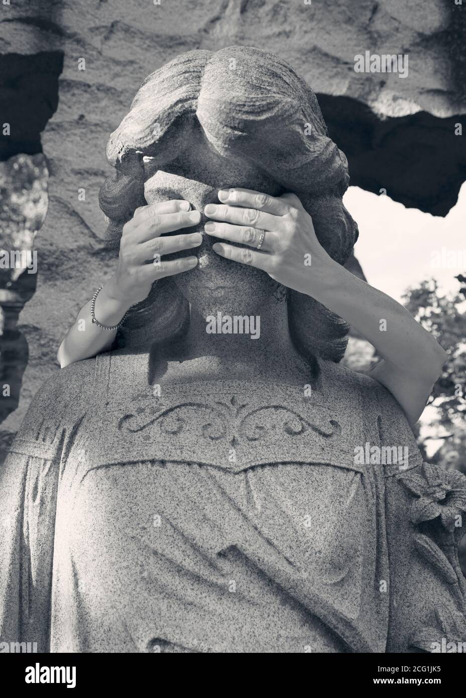 Die Hände einer Frau bedecken die Augen eines Friedhofsengels Statue Stockfoto