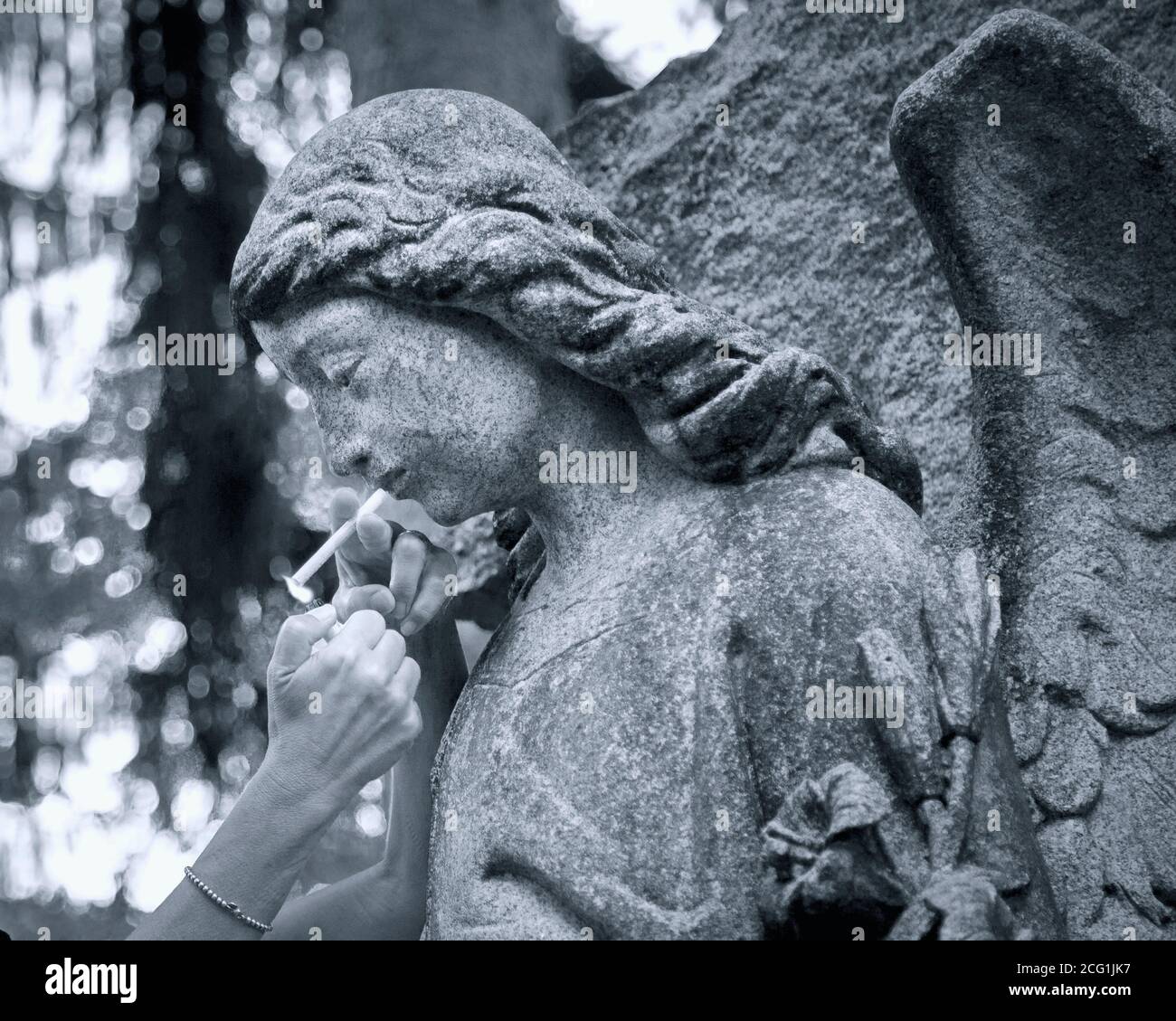 Nahaufnahme einer Frau, die eine Zigarette anzündet Eine Friedhofsengelstatue Stockfoto