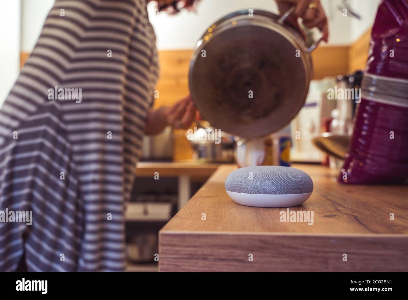 Sprachgesteuerter Smart Speaker in einem Zuhause mit Sprachsteuerung Smart Speaker in einer Innenraumumgebung mit einer Frau Kochen im Hintergrund Stockfoto