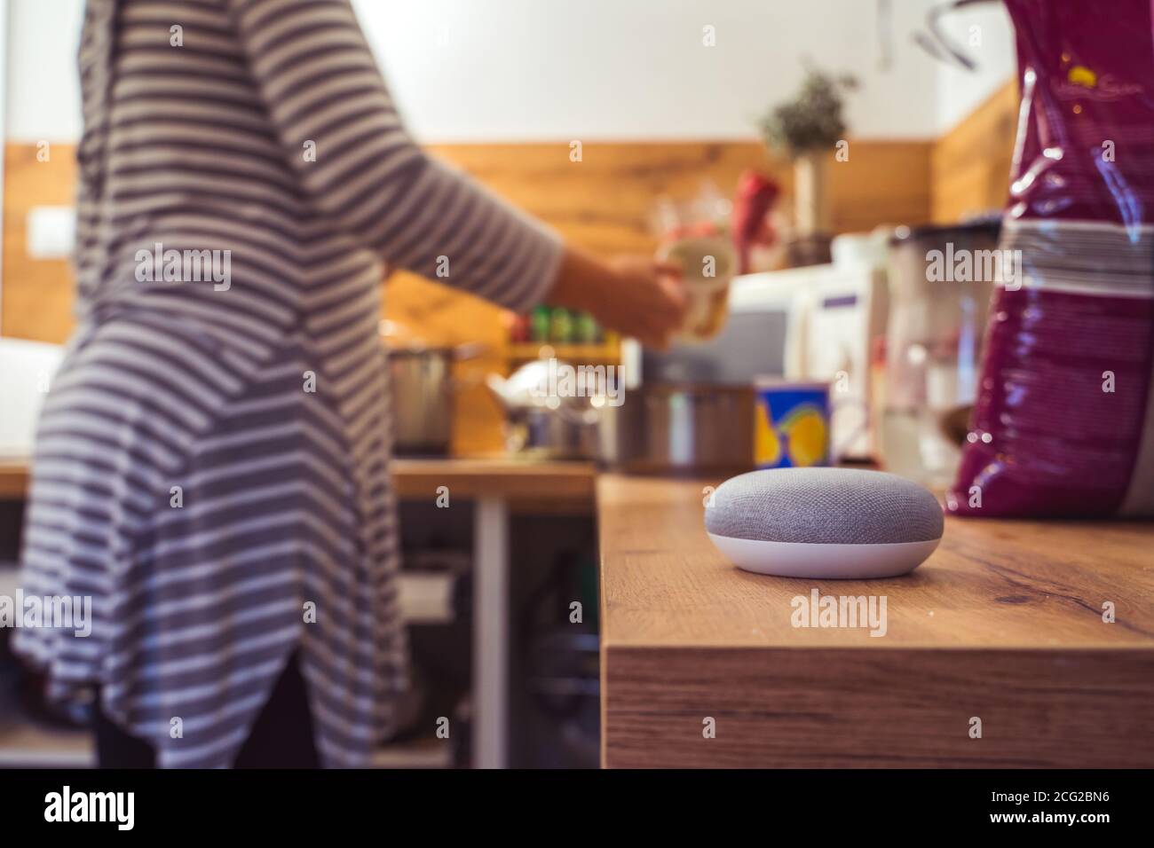 Sprachgesteuerter Smart Speaker in einem Zuhause mit Sprachsteuerung Smart Speaker in einer Innenraumumgebung mit einer Frau Kochen im Hintergrund Stockfoto