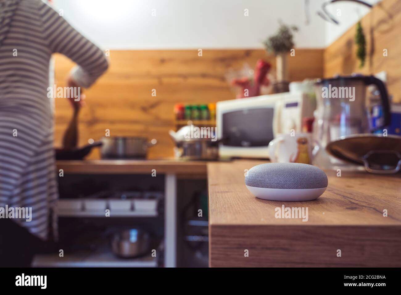 Sprachgesteuerter Smart Speaker in einem Zuhause mit Sprachsteuerung Smart Speaker in einer Innenraumumgebung mit einer Frau Kochen im Hintergrund Stockfoto