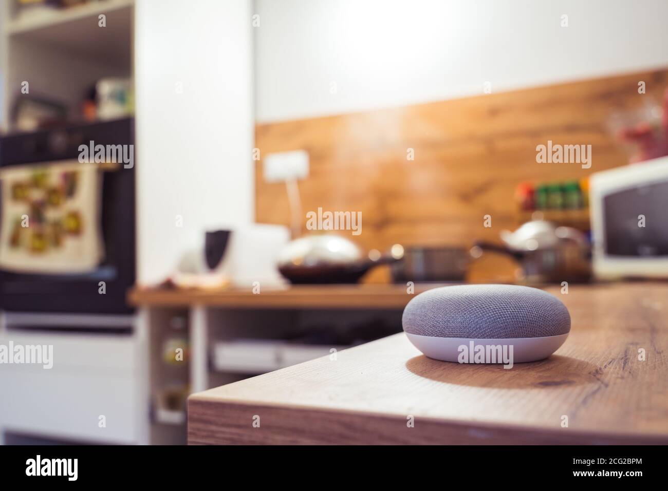 Sprachgesteuerter Smart Speaker in einem Zuhause mit Sprachsteuerung Smart Speaker in einer Innenraumumgebung mit einer Frau Kochen im Hintergrund Stockfoto