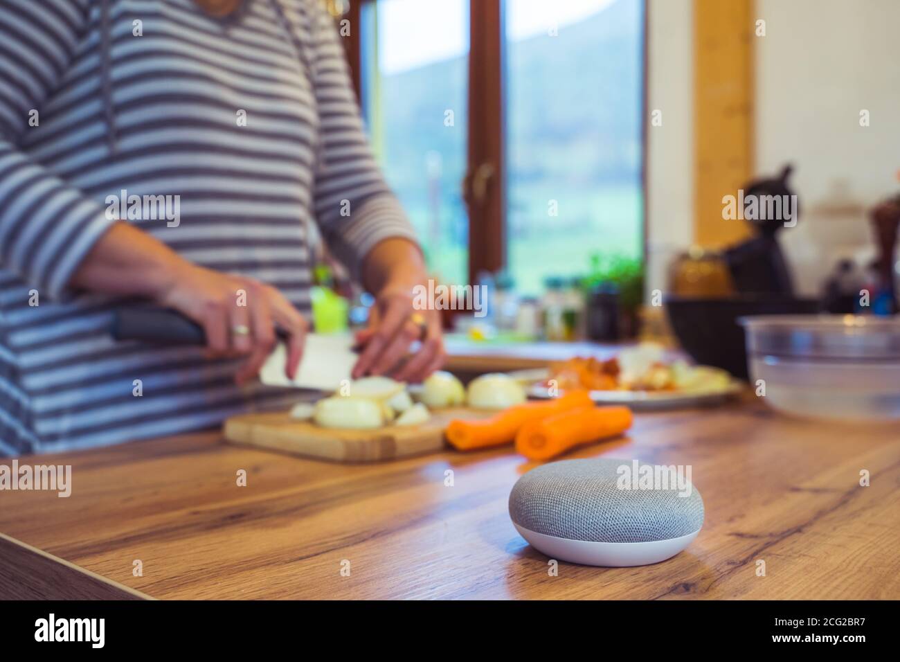 Sprachgesteuerter Smart Speaker in einem Zuhause mit Sprachsteuerung Smart Speaker in einer Innenraumumgebung mit einer Frau Kochen im Hintergrund Stockfoto